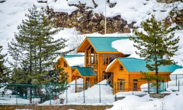 Snow-covered wooden chalet in Pahalgam amid picturesque winter scenery.