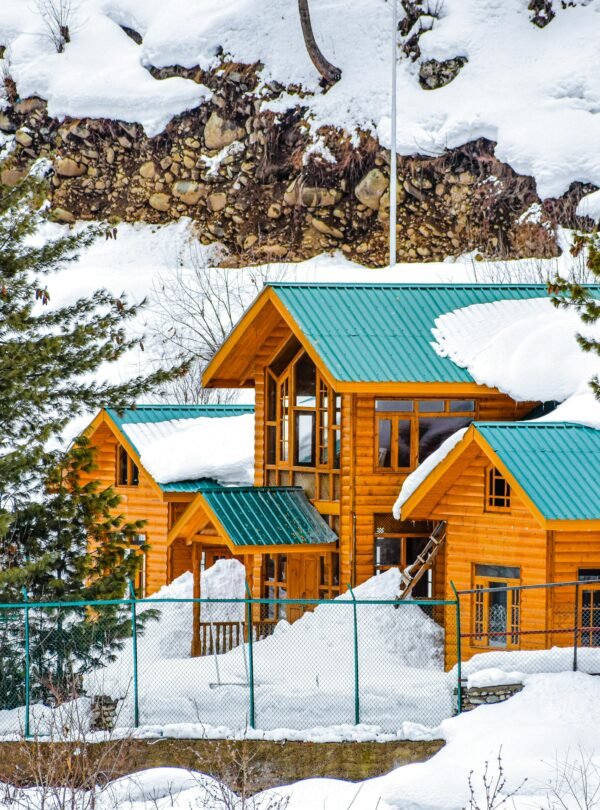 Snow-covered wooden chalet in Pahalgam amid picturesque winter scenery.